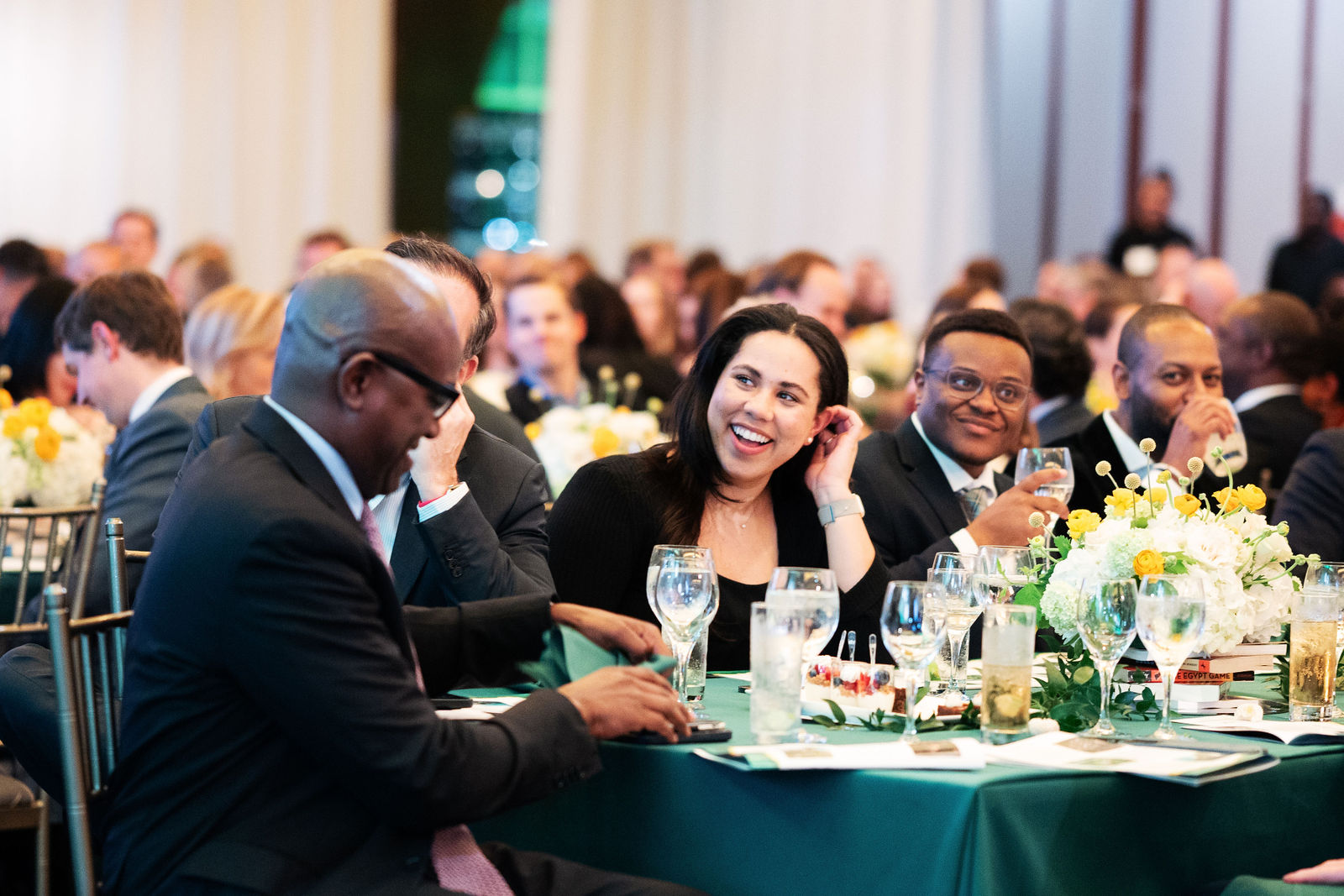 A group of attendees seated at an event table laugh and converse with one another.