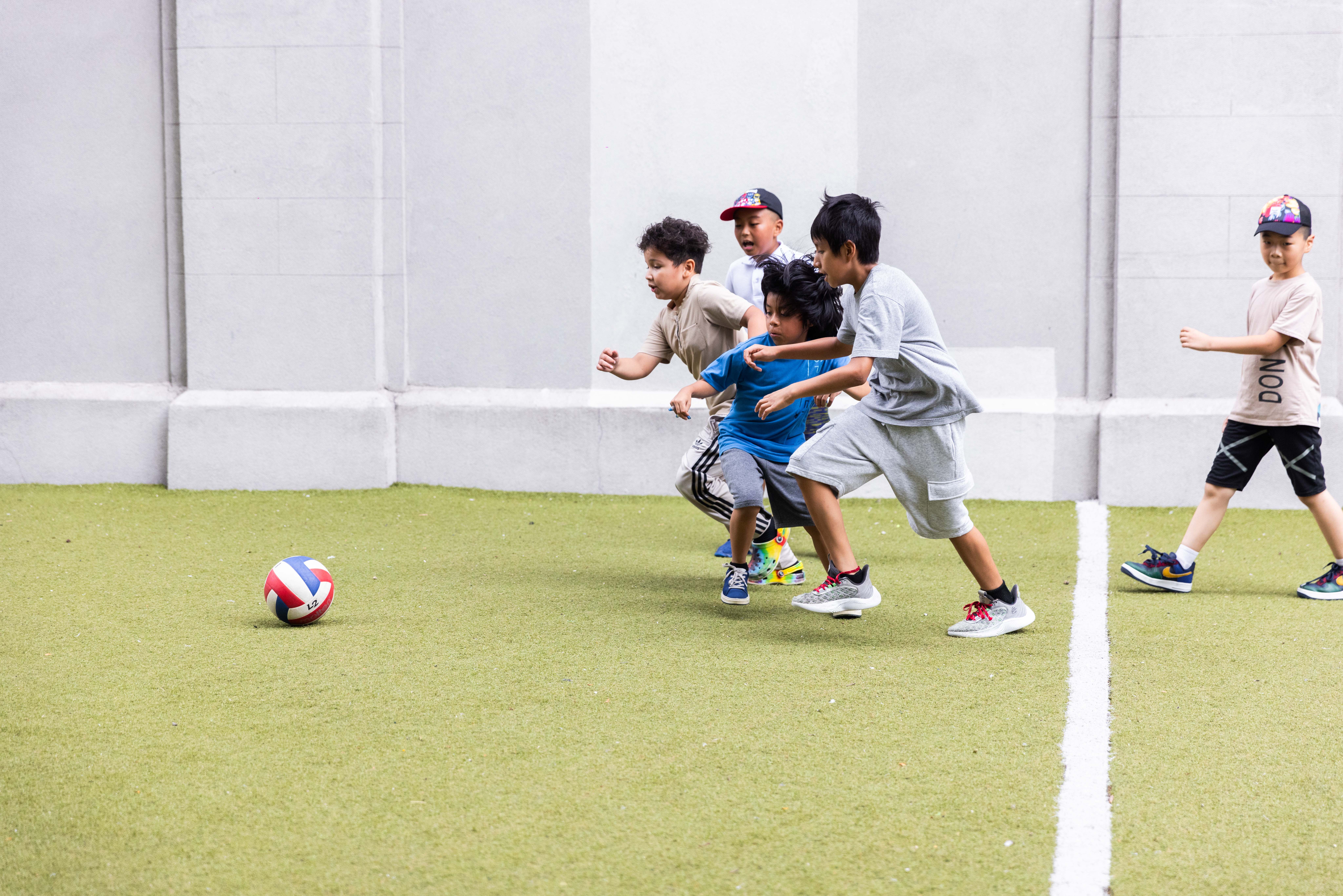 A group of children run after a ball on a soccer field.