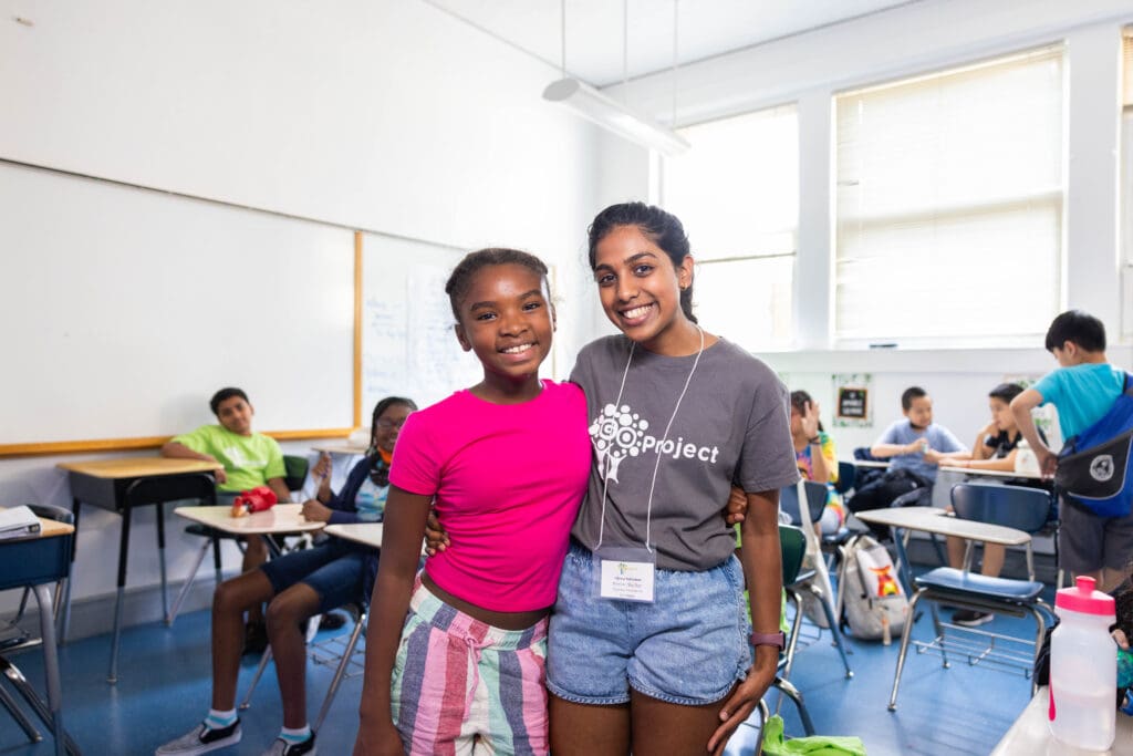 A young student stands with a GO Project volunteer and smiles.