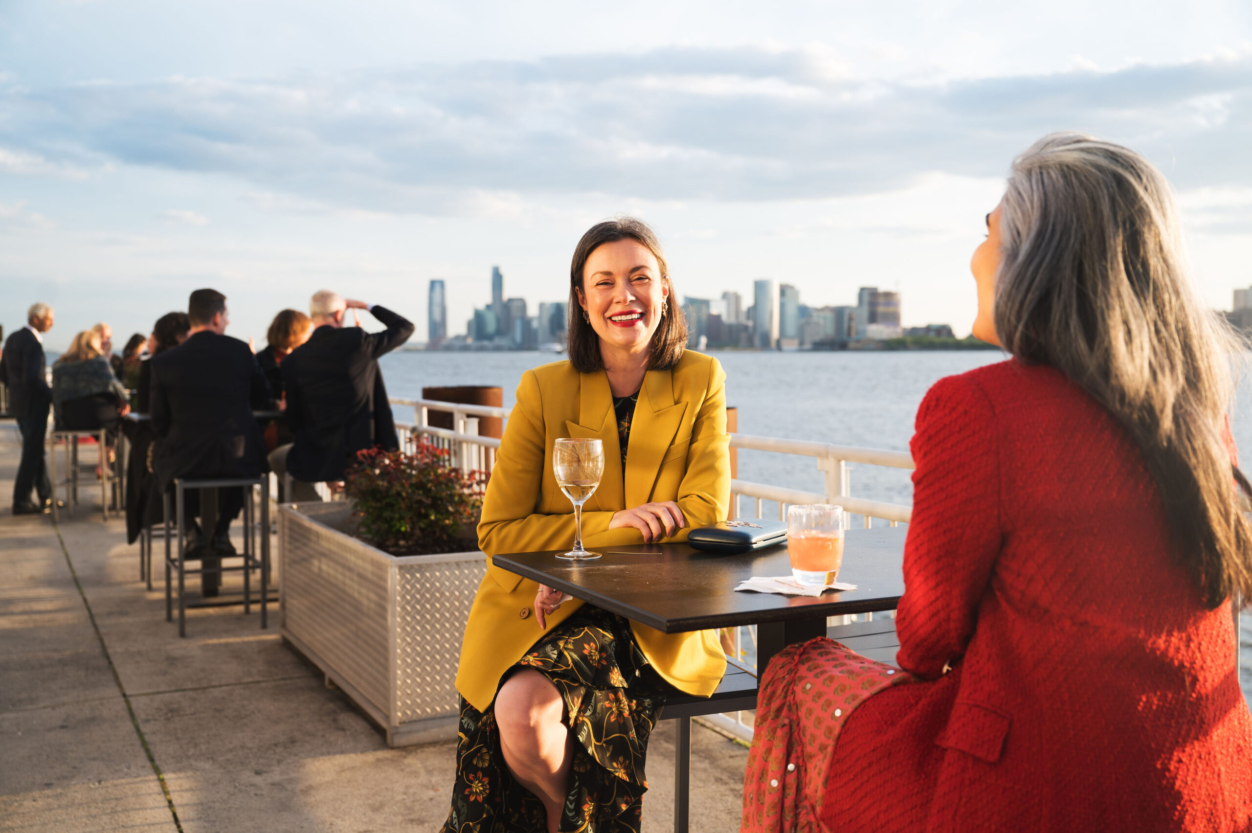 Woman sitting at a table. She is dressed in a yellow and smiling.