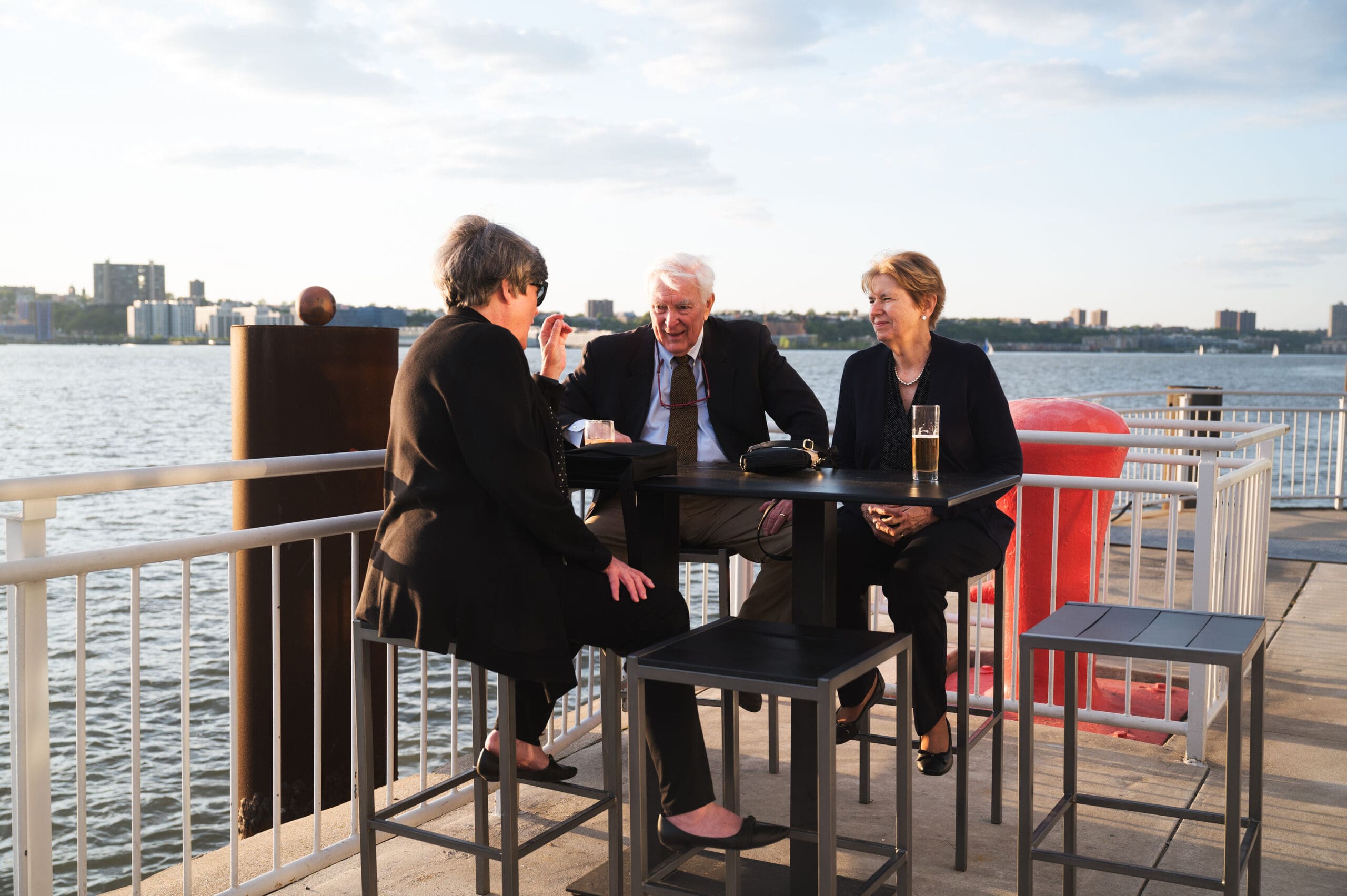 A group of attendees sit at a table on a pier conversing with one another.
