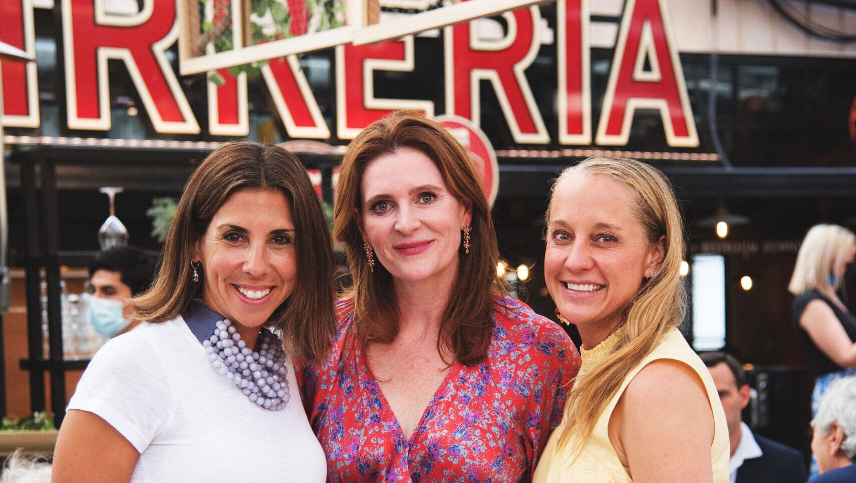 Three women stand together and smile.