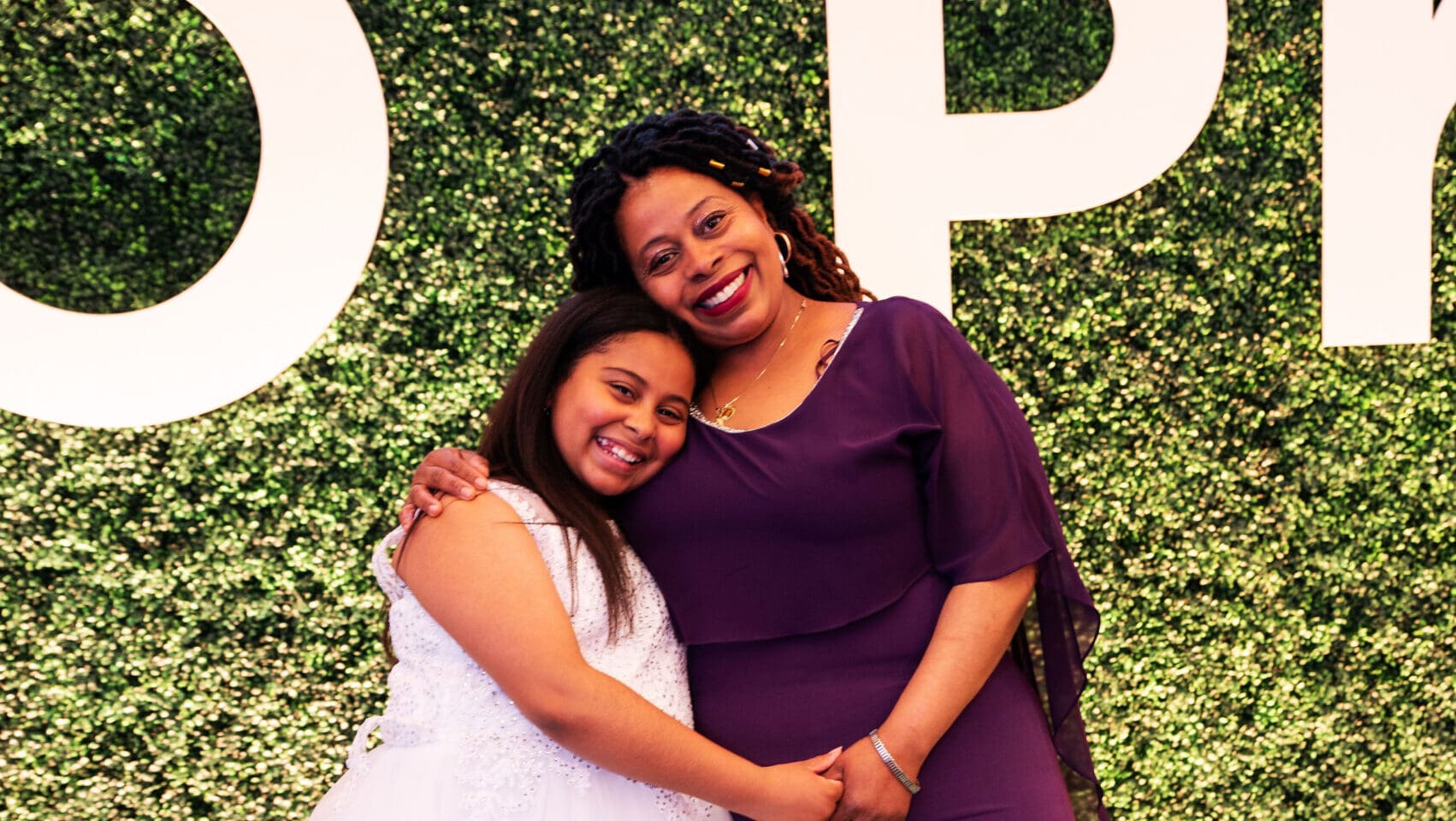 A young girl and her mother smile cheerfully with their arms around each other.