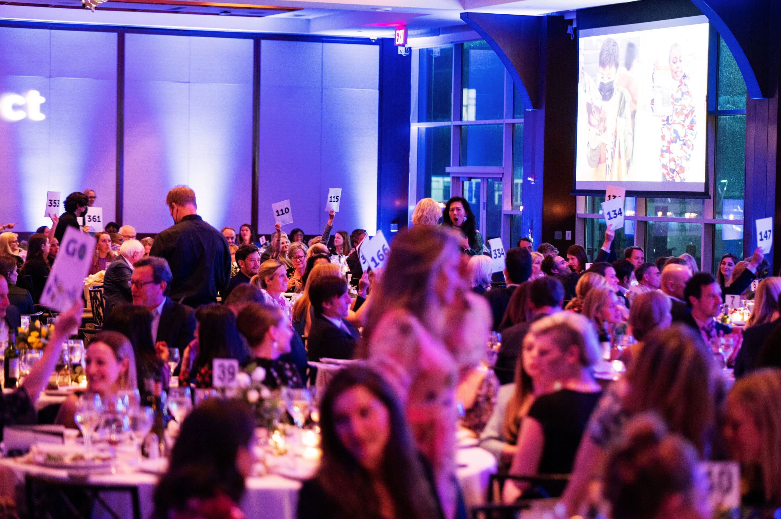 Groups of attendees seated at round party tables participate in an auction.