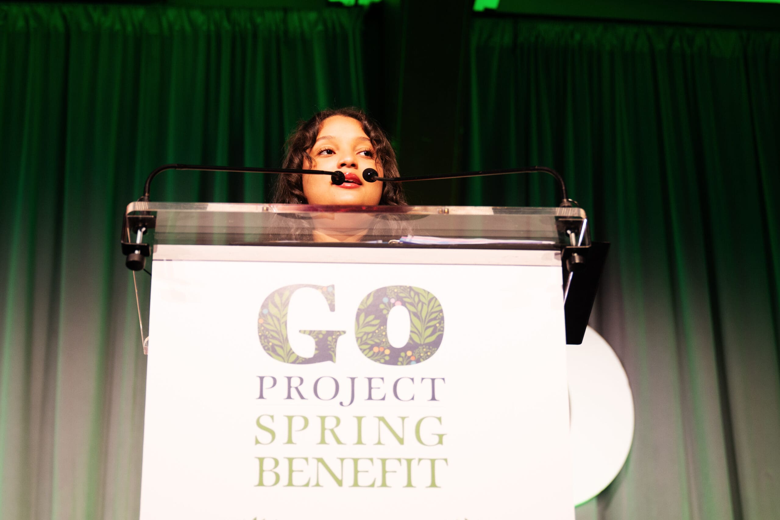 A young girl speaks into a podium mic at the GO Project Spring Benefit.