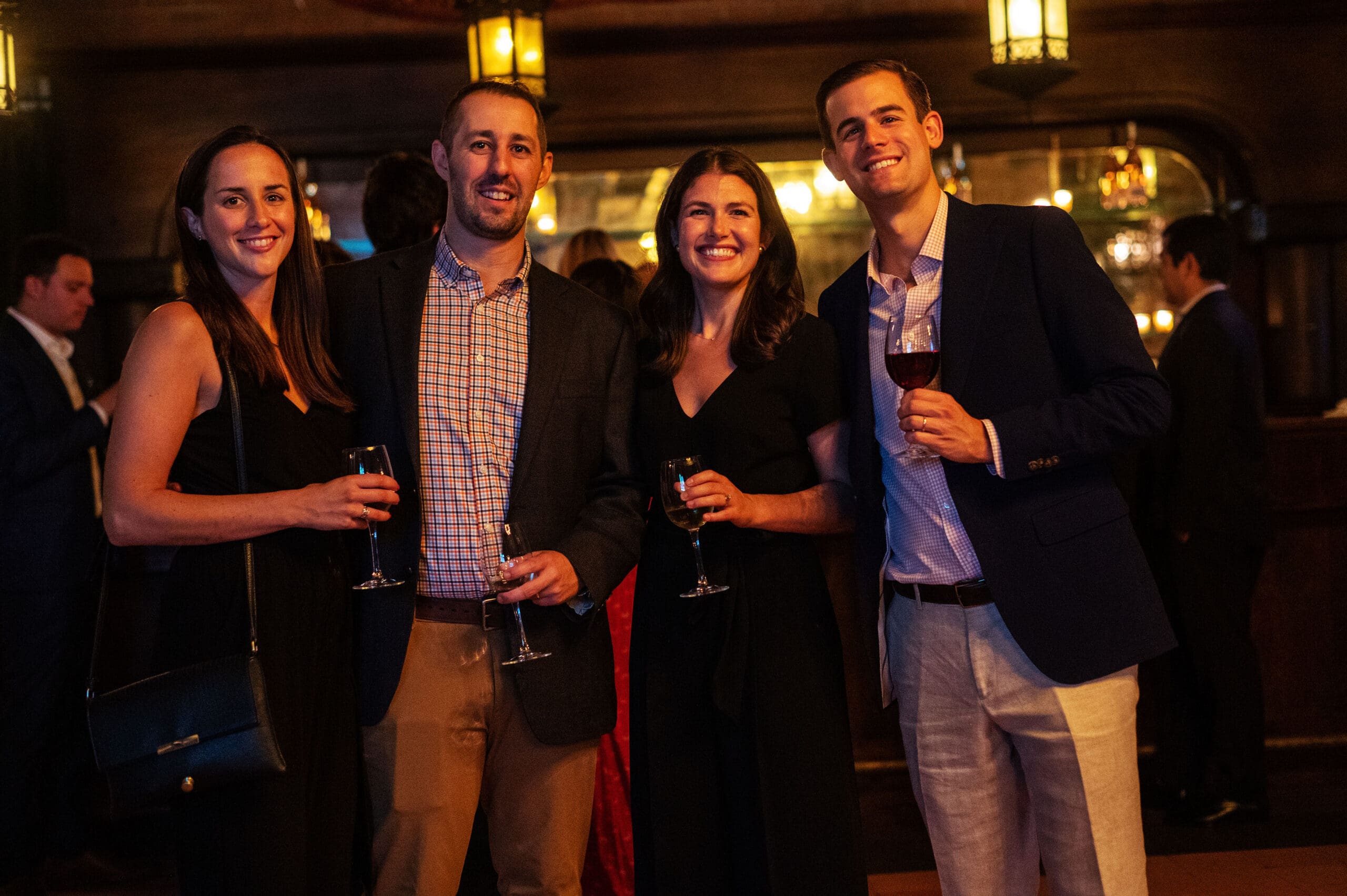 Two men and two women stand together holding wine glasses and smile.