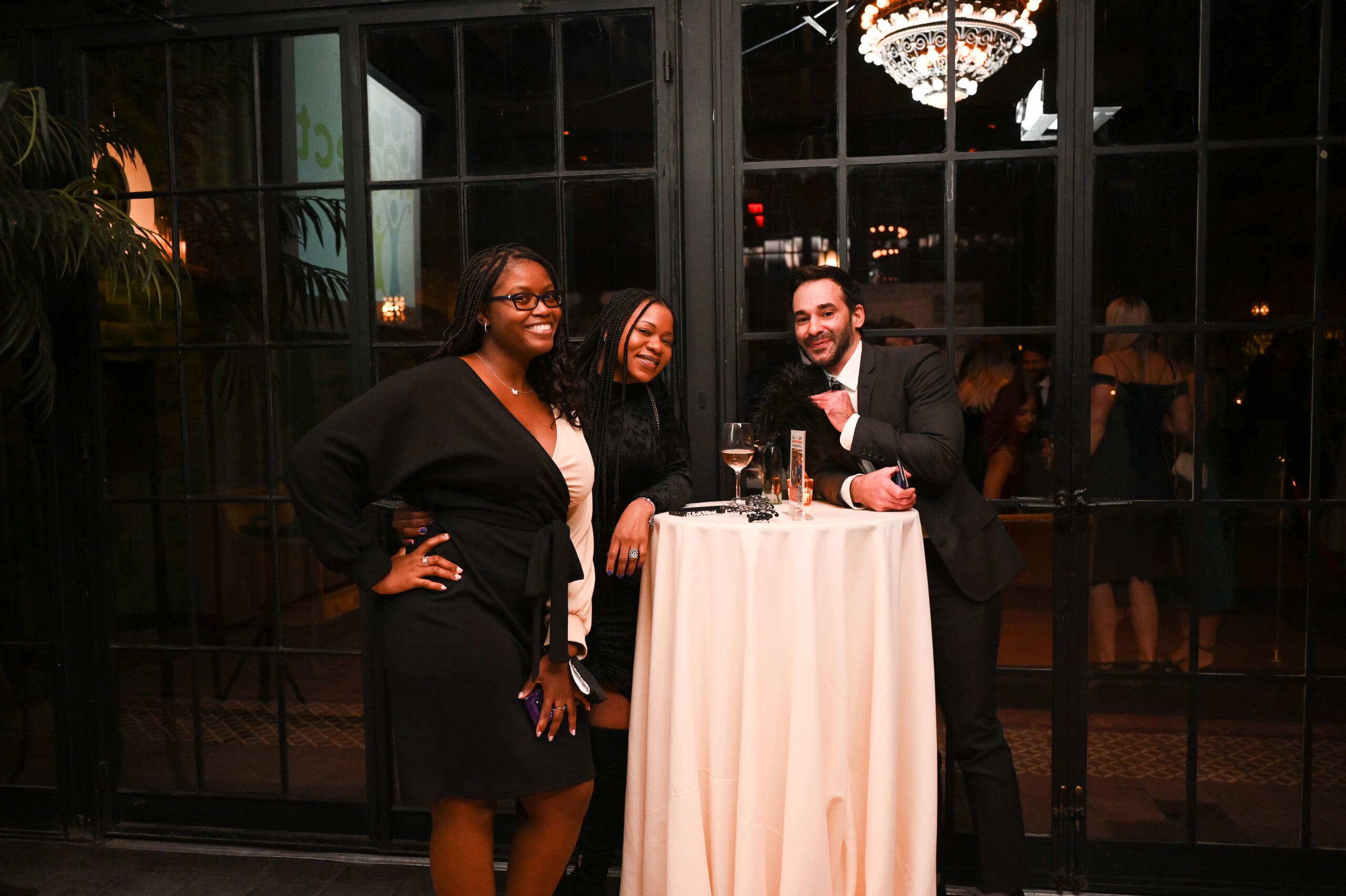 Two women and one man stand at an event table and smile.