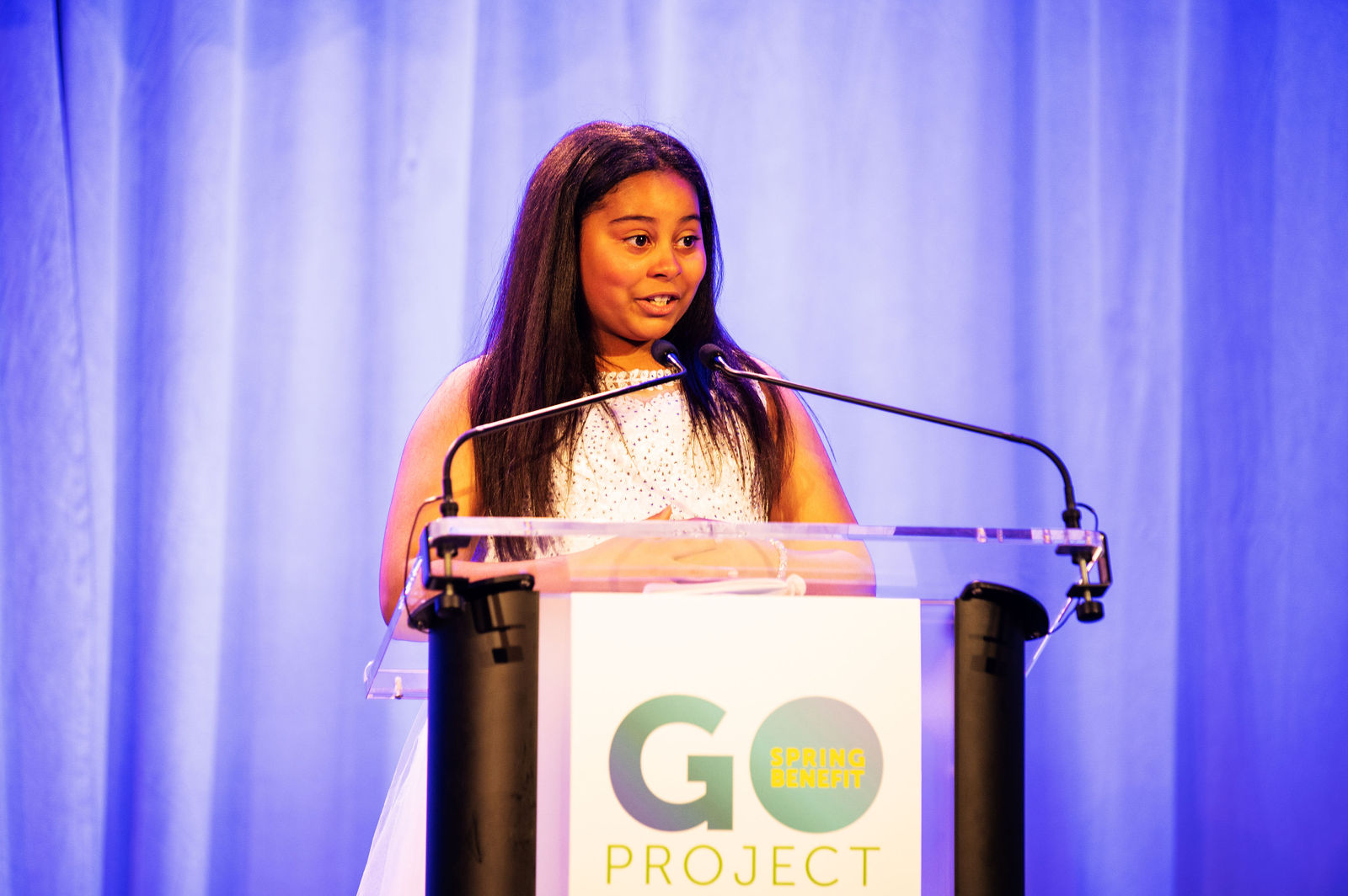A young girl at a podium speaks into the microphone at the GO Project Spring Benefit.