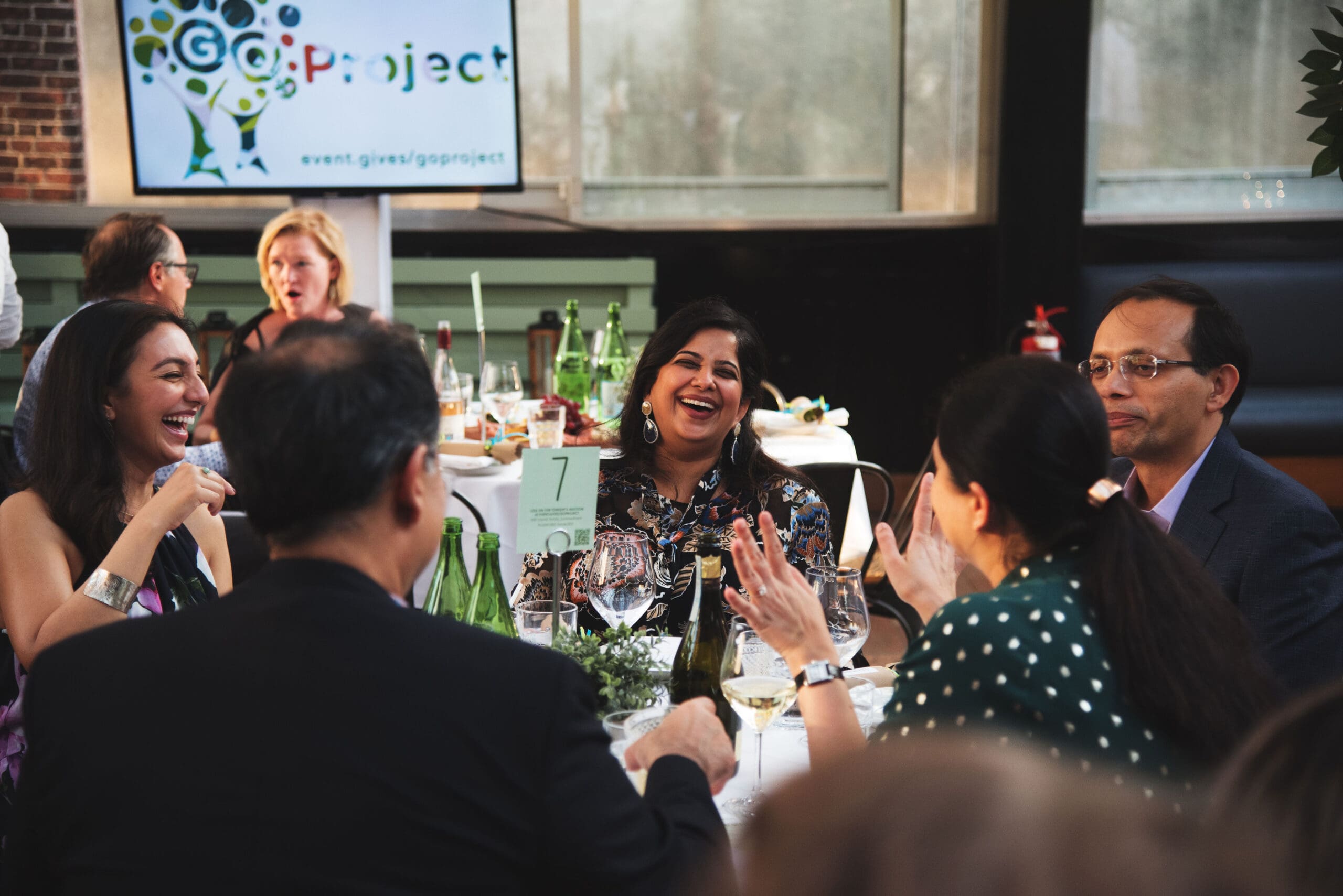 A group of attendees at a round event table laugh and converse with one another.