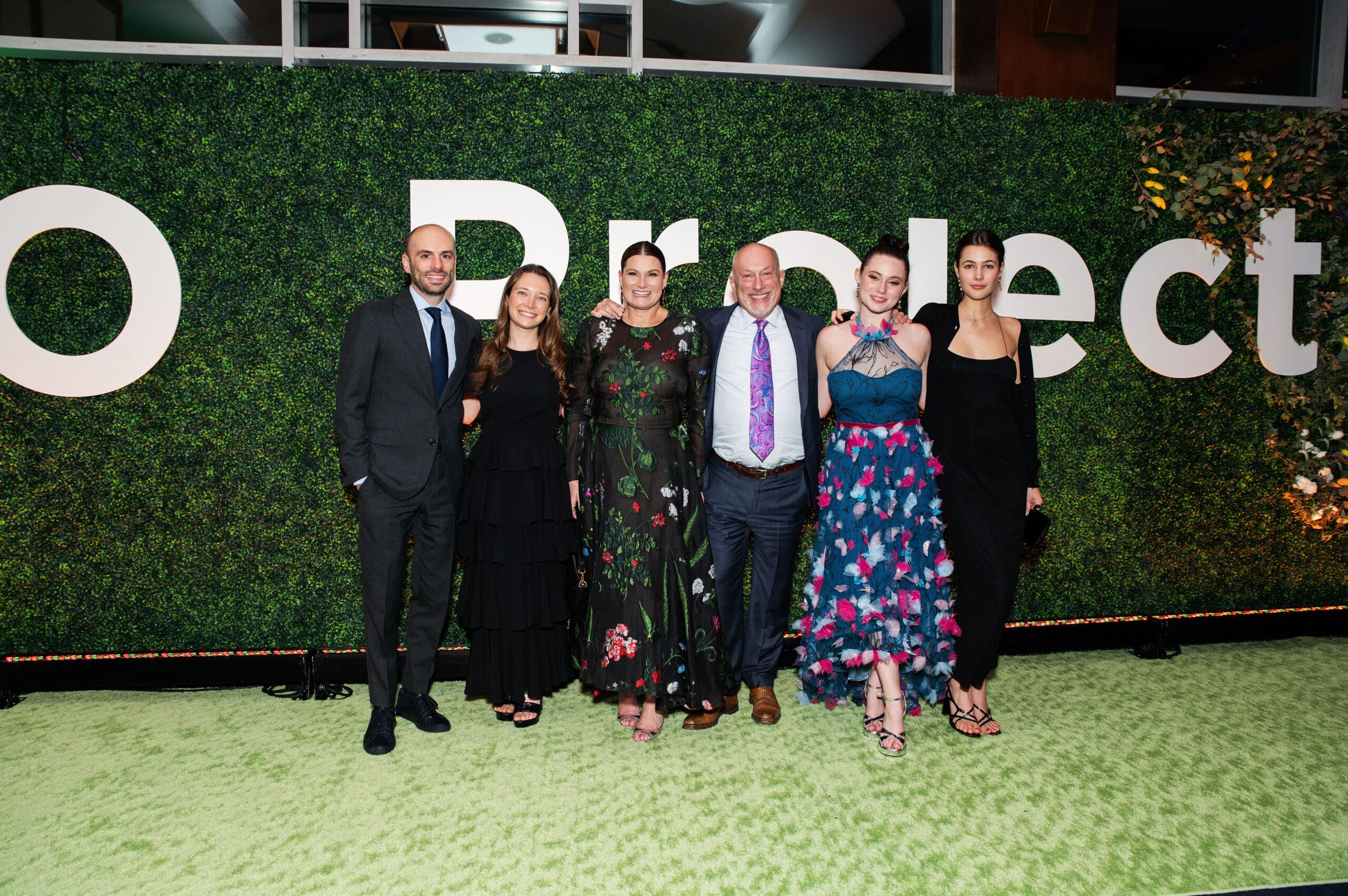 A group of attendees pose in front of a green hedge wall with 'GO Project' lettering.