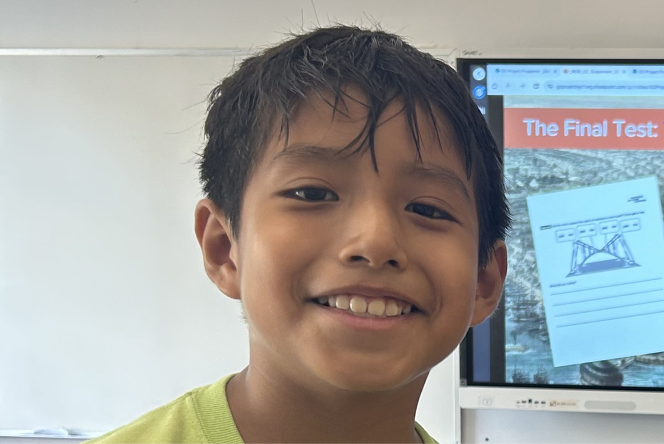 Abraham smiles in front of a whiteboard in a classroom.