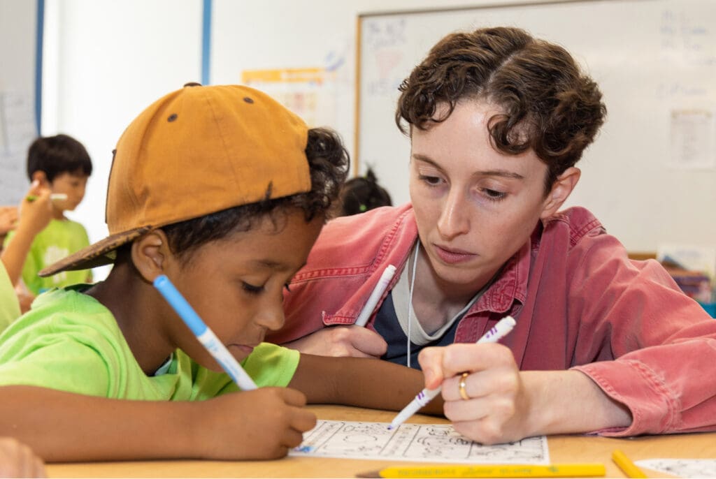 An instructor and a student work an a worksheet together at a desk in a classroom.
