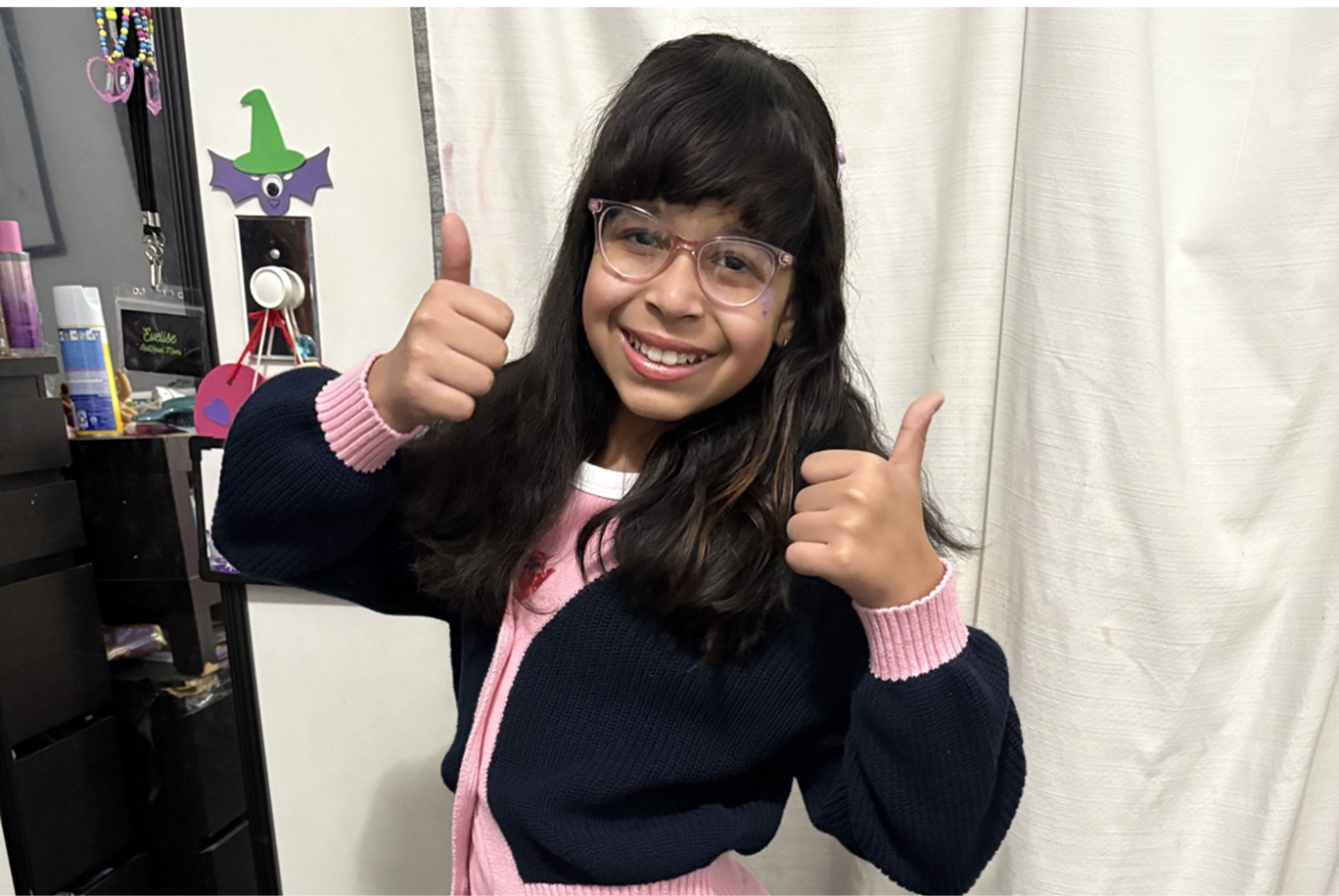 Kali holds two thumbs up and smiles.