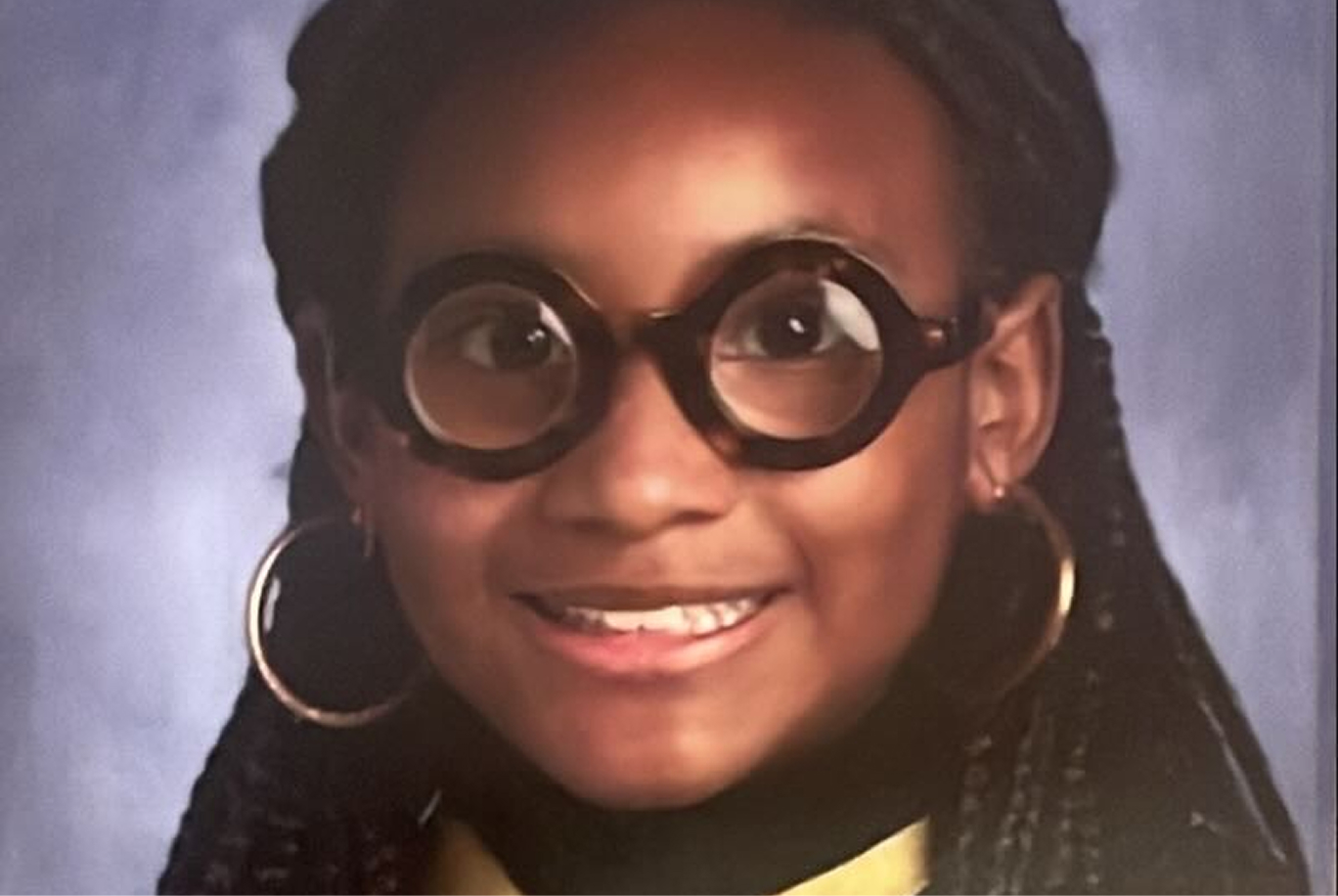 Leila, a young girl, smiles in round tortoiseshell glasses.