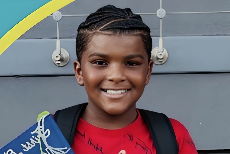 Micah smiles in a red shirt with a black backpack on his shoulders.