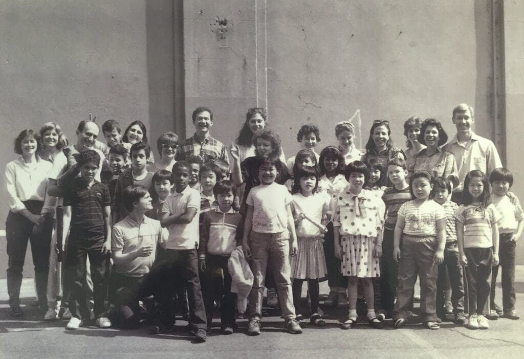 A group of students smile with their teachers and volunteers in a historical photograph.