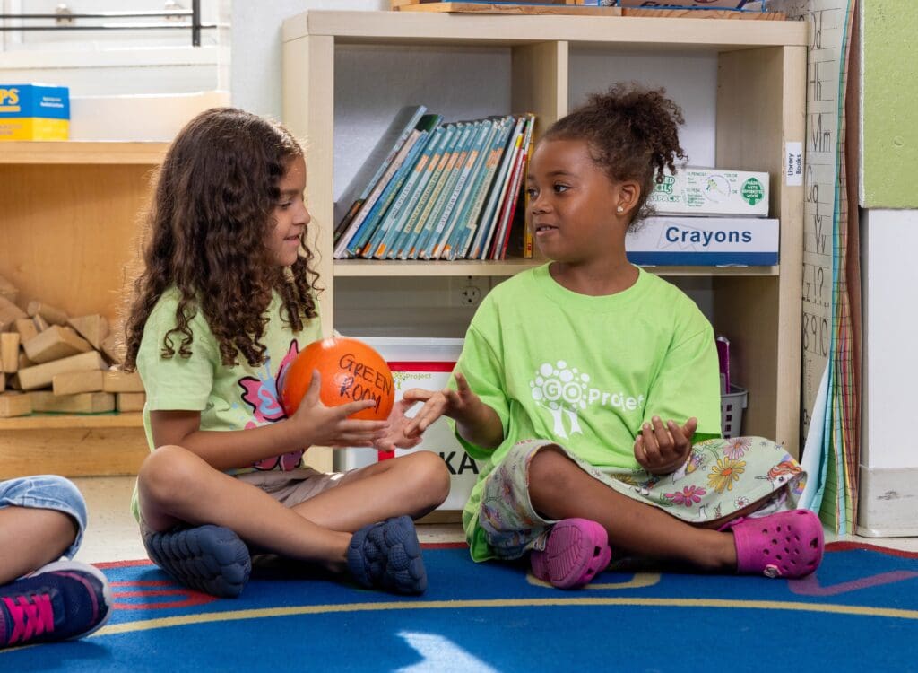 Two young students converse with each other in a classroom.