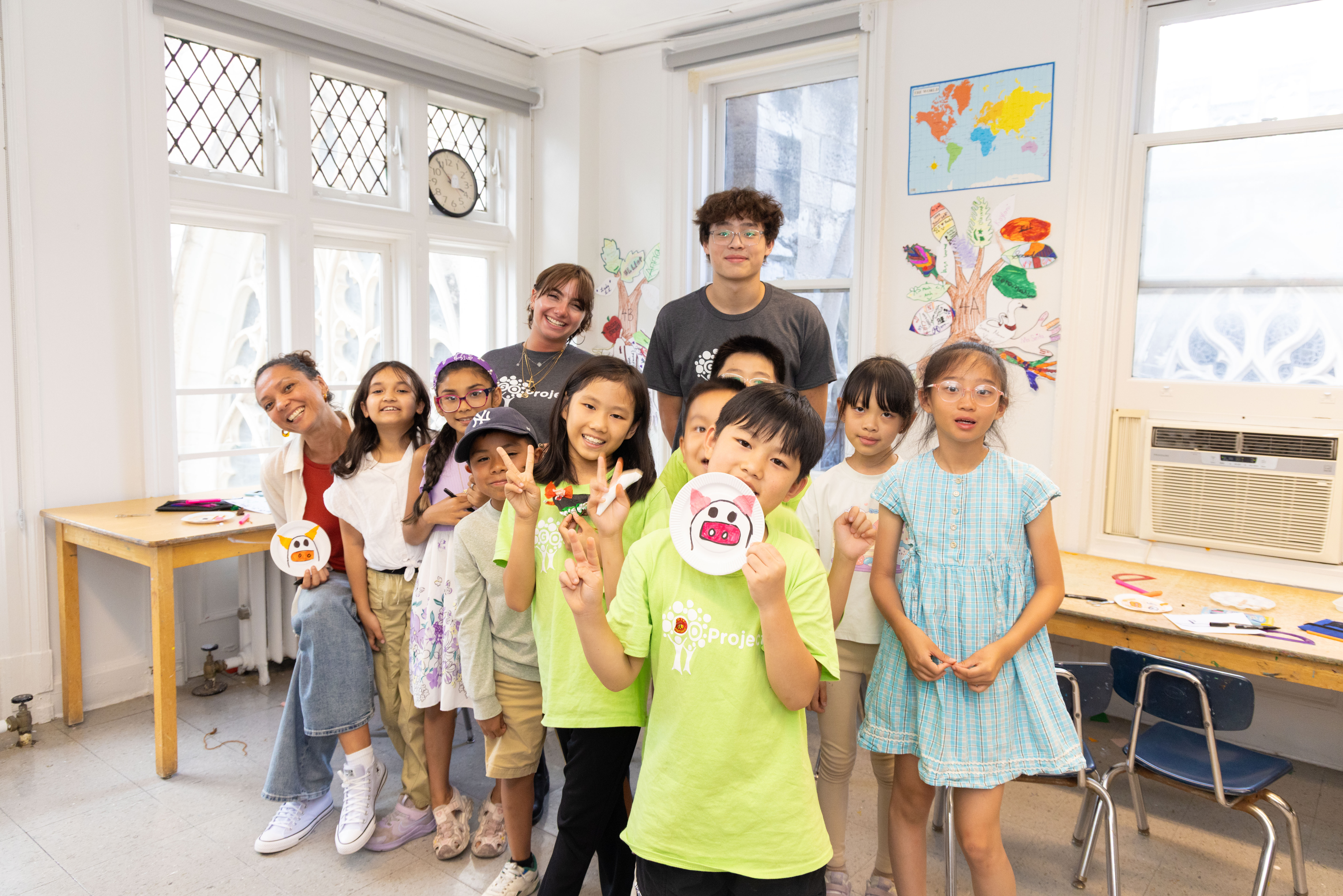 A group of students smile and hold up artwork with their instructor and GO Project volunteers.