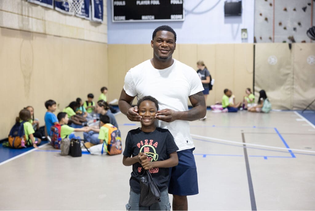 A man poses playfully with a young student in a gymnasium.