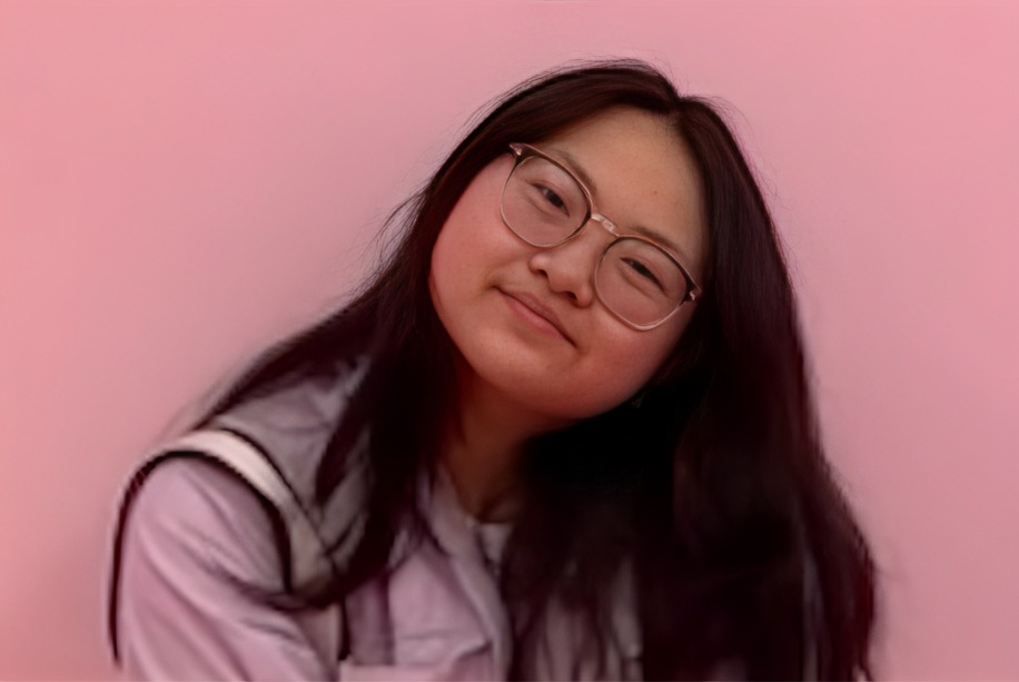 Yumi smiles in front of a pink background.